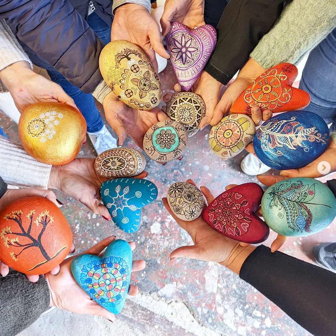 a group of womens hands all holding painted stones and hearts